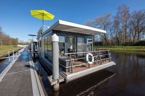 Une structure flottante moderne dotée d’une terrasse couverte, de murs en verre et d’une bouée de sauvetage.