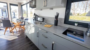 Une cuisine moderne dotée d’une grande fenêtre, d’appareils électroménagers en acier inoxydable et d’un coin repas avec une table et des chaises en verre.