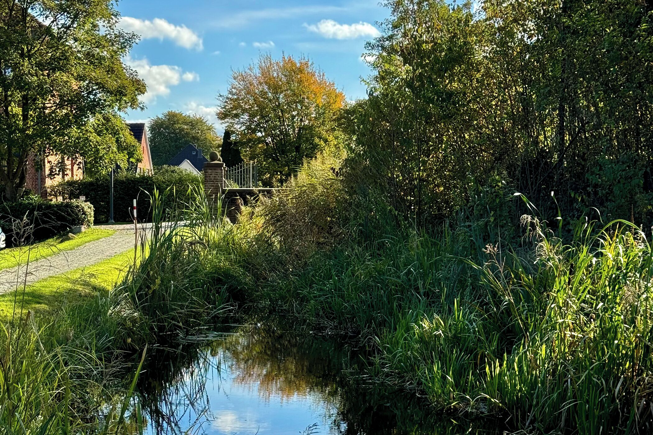 A serene canal with lush greenery and a brick building in the background.
