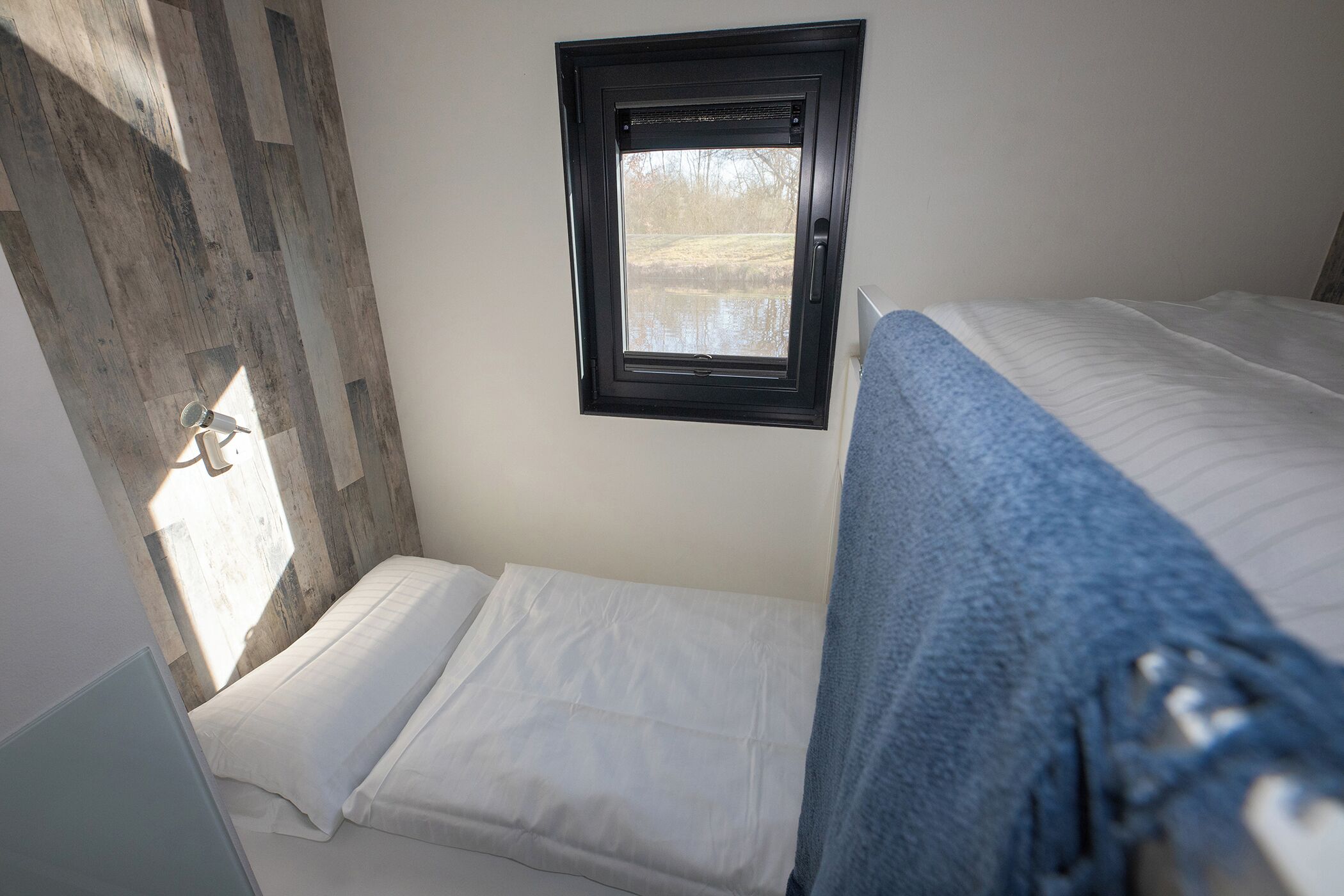 A bedroom with a window, a bed with white bedding, and a wooden wall panel.