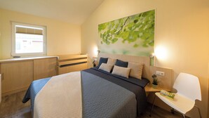 Ein Schlafzimmer mit Bett, Nachttisch, Lampe und einem Fenster mit Jalousien.