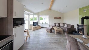 Eine moderne Küche mit eingebauten Geräten, ein Essbereich mit Tisch und Stühlen, ein Wohnzimmer mit Sofa und Kamin, sowie große Fenster für natürliches Licht.