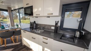 A modern kitchen with white cabinets, a stainless steel sink, and a window with blinds. - Houseboat 7 Starfish. Picturesque by the lake and unconventional. (Geestland)