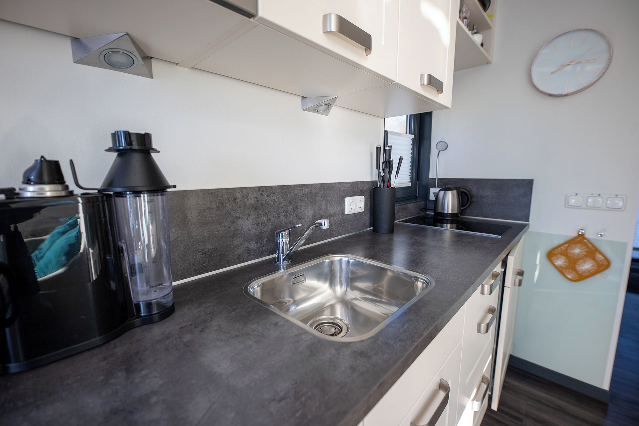 A modern kitchen with a stainless steel sink, a coffee maker, and a kettle.