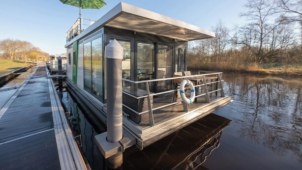 Una casa flotante con cubierta techada, paredes de vidrio y un flotador.