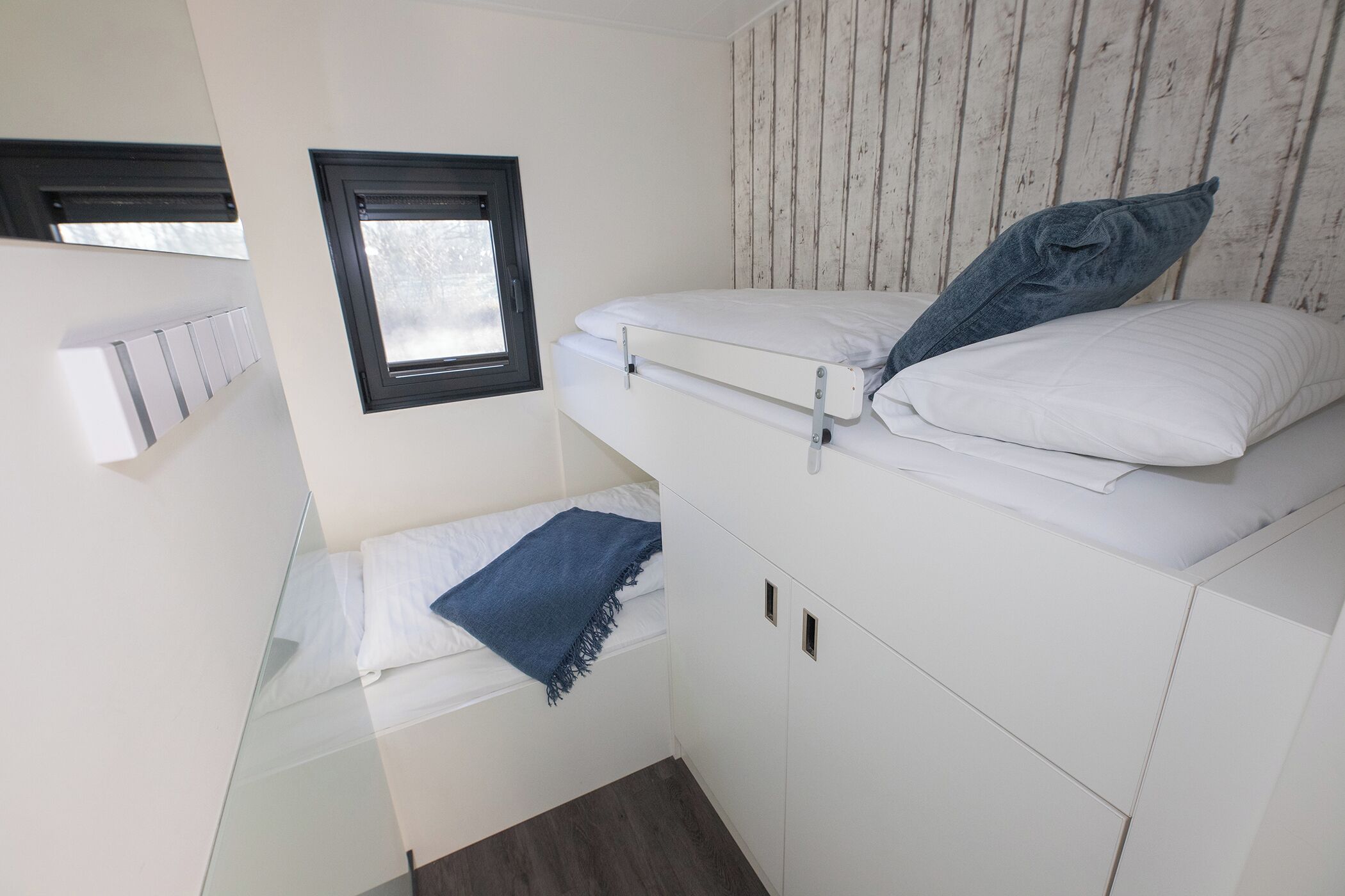 A compact room with a bunk bed, a small window, and a built-in wardrobe.