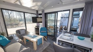Una sala moderna con un sofá, sillones, una mesa de centro y un comedor con una mesa dispuesta para dos.