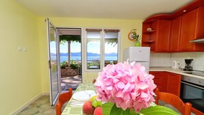 A dining area with a table set for two, a view of the outdoors, and a kitchen with red cabinets.