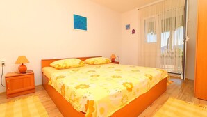 A bedroom with a large bed, two bedside tables, a nightstand, a window with curtains, and a door.