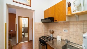 Een compacte keuken met een gasfornuis, een inbouwoven, een roestvrijstalen spoelbak, houten kastjes en een koffiezetapparaat op een plank.