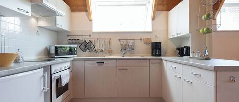 A modern kitchen with white cabinets, a wooden ceiling, and a window above the sink.