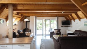 A spacious living area with a high ceiling, wooden beams, a sofa, a TV, and a dining area with chairs and a table.