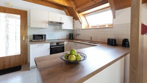 A kitchen with white cabinets, a wooden countertop, a bowl of green apples, a microwave, a toaster, and a window with natural light.