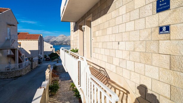 Un immeuble à la façade en pierre, doté d’un balcon avec une balustrade blanche et d’une enseigne indiquant qu’il s’agit d’un appartement.