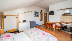 Une pièce de taille modeste comprenant un lit, un bureau, une chaise, une petite kitchenette et un téléviseur fixé au mur.