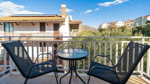 Un balcon avec deux chaises et une table, donnant sur un quartier résidentiel avec des immeubles et de la verdure.