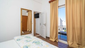 Un dormitorio con cama, espejo, puerta y ventana con cortinas.