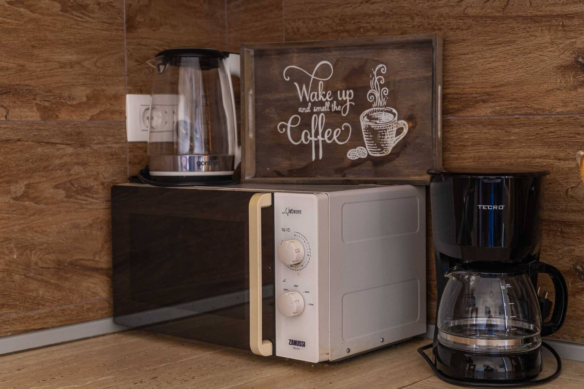 Cuina amb microones, cafetera i un cartell que diu "Despertar i sentir l'aroma del cafè".