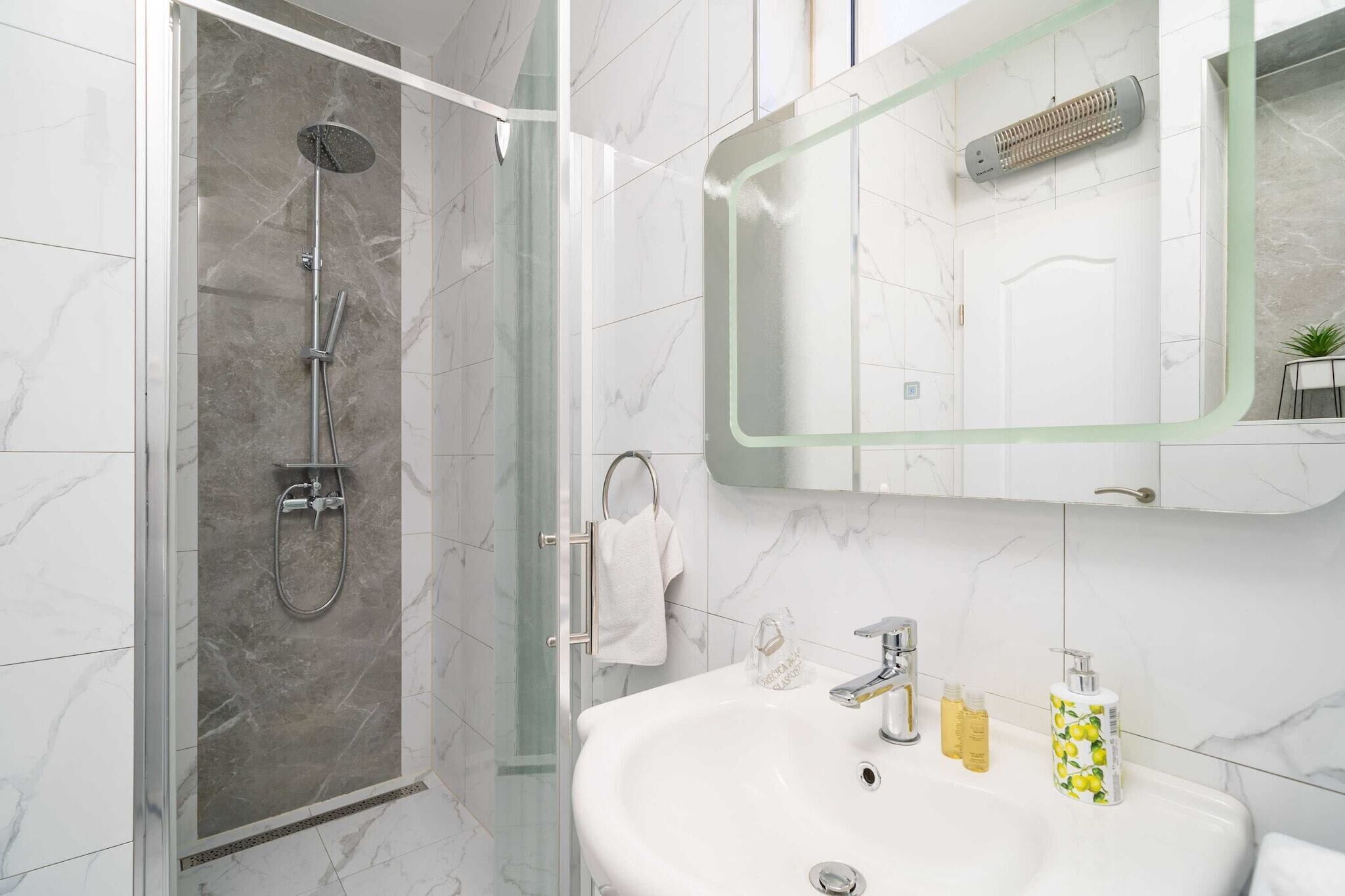 Une salle de bain moderne avec une douche à parois de verre, un lavabo blanc avec deux flacons de savon et un miroir avec un cadre vert.