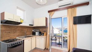 Cocina compacta con estufa, lavamanos y armarios, que da a un balcón con mesa y sillas.