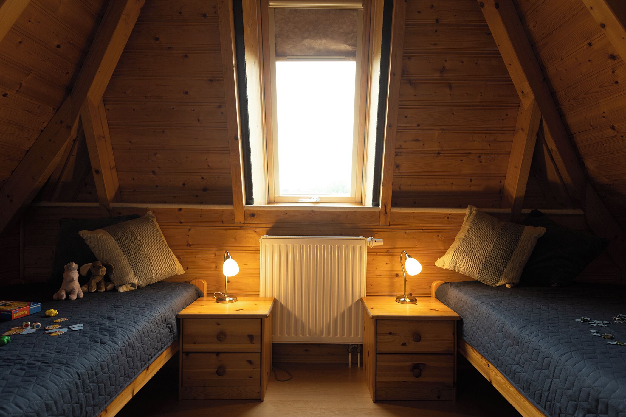 Een gezellige slaapkamer op zolder met twee bedden, houten wanden, een raam en een radiator.