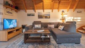 A living room with a wooden ceiling, a large sectional sofa, a TV, and a coffee table. - Vacation home Piratennest. Child-friendly and close to the beach. (Wurster Nordseeküste)