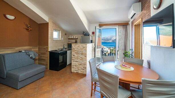 Ein kompakter Wohnbereich mit Küchenzeile, einer Couch, einem Esstisch und einem Balkon mit Meerblick.