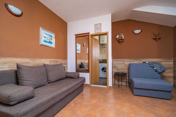 A living room with a sofa, a blue armchair, a washing machine, and a small table. - Apartments Senjo - One Bedroom Apartment with Balcony with Sea View (Apartman 1) (Cavtat)