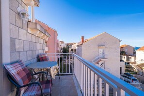 A balcony with a table and chairs, overlooking a street with buildings and a clear sky. - Apartments Senjo - One Bedroom Apartment with Balcony with Sea View (Apartman 1) (Cavtat)