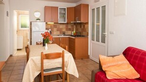 A compact kitchen with wooden cabinets, a dining table with chairs, and a red sofa with an orange pillow.