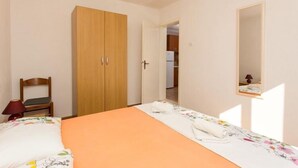 A bedroom with a bed, a wooden wardrobe, a chair, a desk, and a mirror.