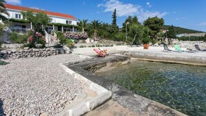 A coastal hotel with a clear pool, stone pathway, and beach chairs.