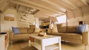 Un amplio salón con techos altos, una escalera, un conjunto de sofás y una cocina al fondo.