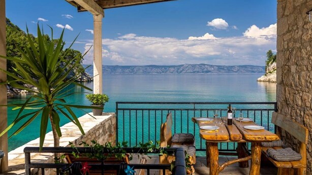 Une terrasse avec une table dressée pour le dîner, offrant une vue sur un plan d’eau et des montagnes.