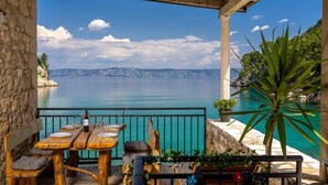 Une terrasse avec une table dressée pour le dîner, offrant une vue sur une mer calme et des montagnes lointaines.