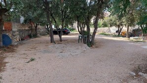 A gravel driveway leading to a parked car, surrounded by trees and a stone wall. - Apartments Paula - One Bedroom Apartment with Terrace 1 (Jezera)