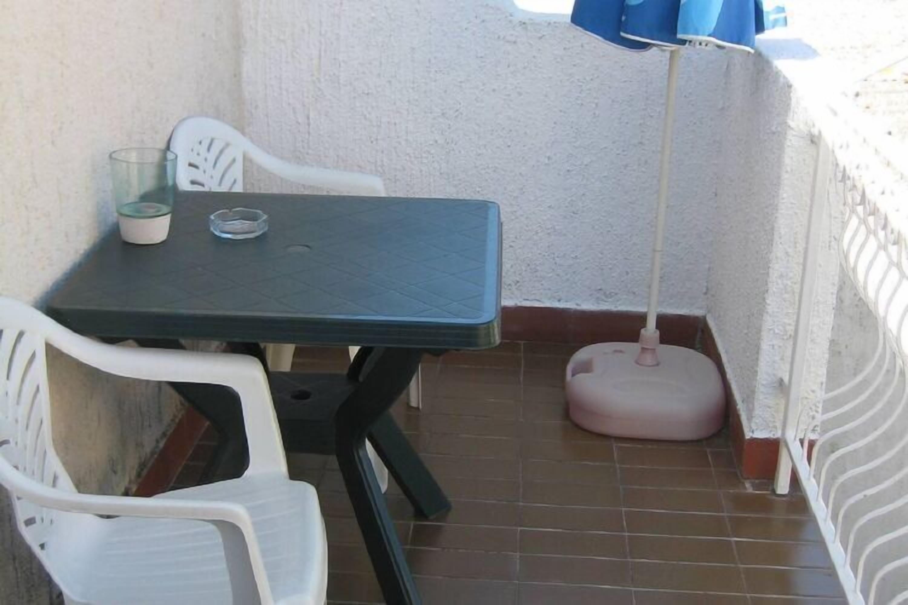 A small balcony with a table and chairs, a floor lamp, and a trash bin.