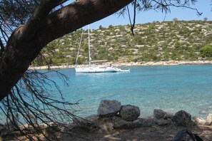 A sailboat on a calm sea with rocky shores and a hilly landscape in the background.