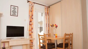 A room with a TV on a stand, a dining table with chairs, and a sliding door with curtains. - Apartments Paula - One Bedroom Apartment with Terrace 1 (Jezera)