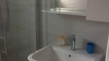 A bathroom with a glass shower enclosure, a white sink with a soap dispenser, and a blue cup.