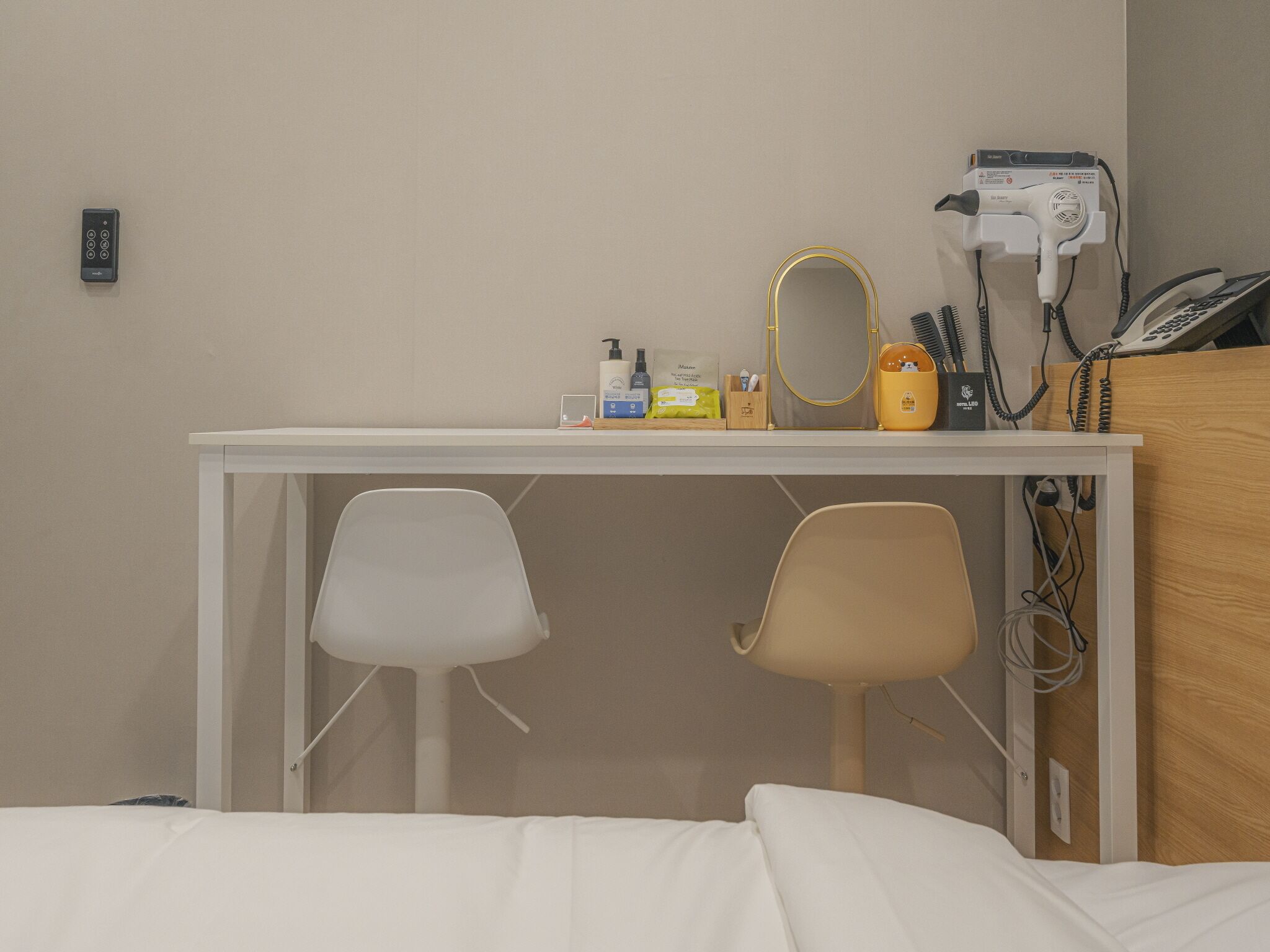 A hotel room with a bed, a desk with two chairs, a hairdryer, a mirror, and a phone.