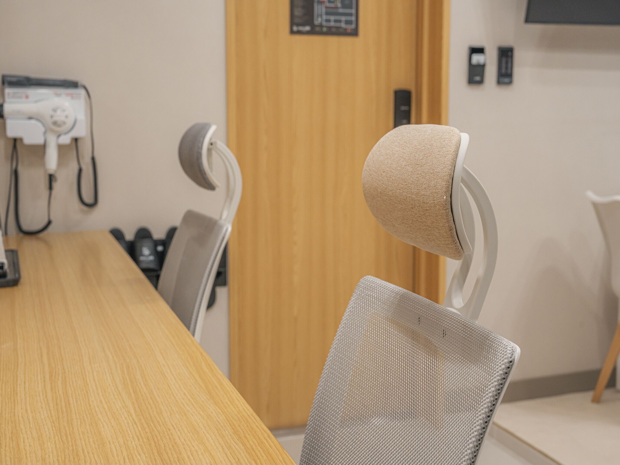 A conference room with a long wooden table, several chairs with fabric headrests, a telephone, and a wooden door in the background.