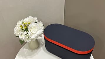 A white vase with white flowers and a black and red box on a white surface.