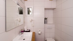 A modern bathroom with a white sink, mirror, and shower. There is a small window above the mirror and a towel rack on the wall. - Lavender Garden Apartments - Studio Apartment (First Floor) - APT 3 (Dubrovnik)