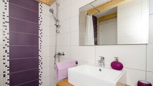 A bathroom with a white sink, purple soap dispenser, and a shower with a purple tiled wall. - Lavender Garden Apartments - Studio Apartment (First Floor) - APT 3 (Dubrovnik)
