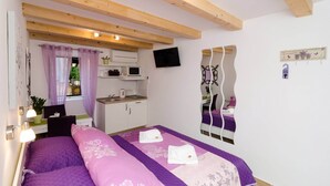 A bedroom with a bed, a desk, a mirror, and a window with curtains. - Lavender Garden Apartments - Studio Apartment (First Floor) - APT 3 (Dubrovnik)