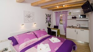 A bedroom with a bed, a desk, a chair, a small kitchenette, and a TV. - Lavender Garden Apartments - Studio Apartment (First Floor) - APT 3 (Dubrovnik)
