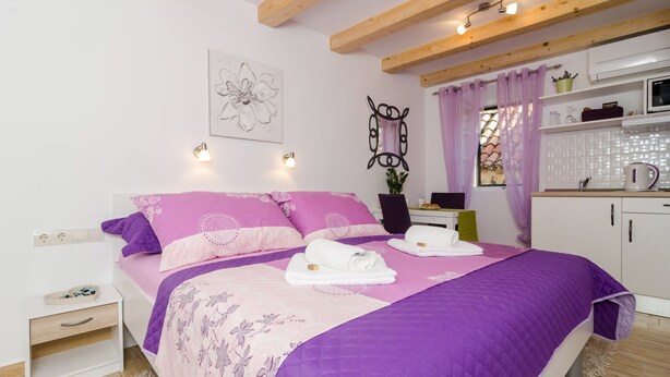 A bedroom with a bed, bedside table, and a small kitchenette area. - Lavender Garden Apartments - Studio Apartment (First Floor) - APT 3 (Dubrovnik)