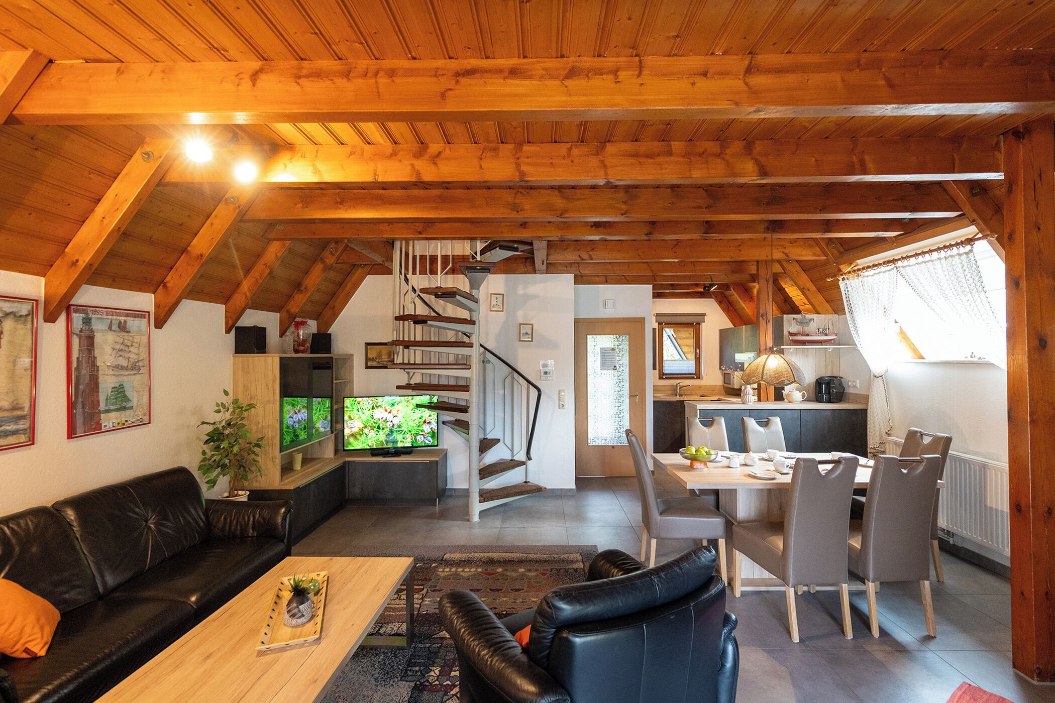A spacious living area with a wooden ceiling, a black leather sofa, a wooden coffee table, and a dining area with chairs and a table.