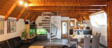 Un vaste espace de vie doté d’un plafond en bois, d’un canapé en cuir noir, d’une table basse en bois et d’un coin repas avec des chaises et une table.